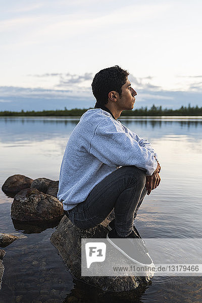 Finland  Lapland  man sitting on a rock in a lake