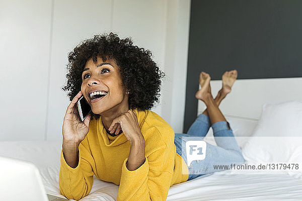 Glückliche Frau liegt im Bett und telefoniert mit dem Handy