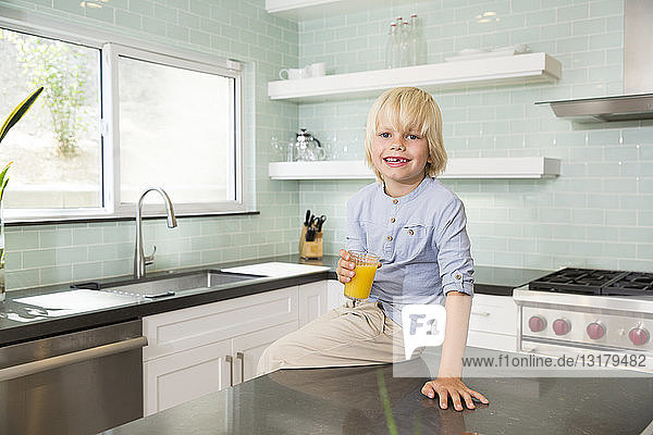 Porträt eines glücklichen Jungen in der Küche mit einem Glas Orangensaft