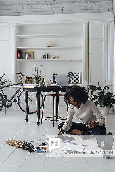 Disignerin  die auf dem Boden ihres Heimbüros sitzt und ein digitales Tablet benutzt