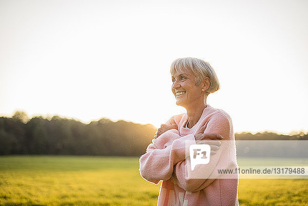 Smiling senior woman standing on rural meadow at sunset