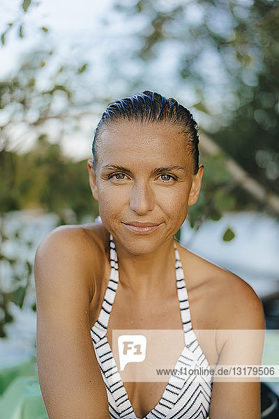 Porträt einer lächelnden Frau mit nassem Haar im Bikini an einem See
