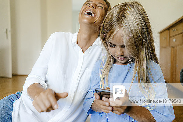 Lachende Mutter und Tochter schauen auf Smartphone