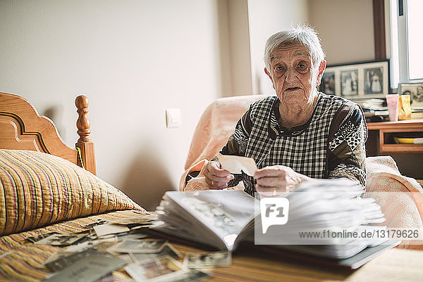 Porträt einer älteren Frau  die zu Hause alte Fotos in ein Fotoalbum legt