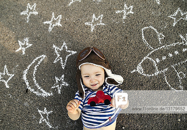 Porträt eines lächelnden Mädchens mit Pilotenhut auf Asphalt liegend  bemalt mit Flugzeug  Mond und Sternen
