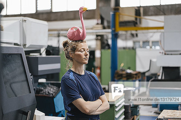 Junge Frau arbeitet als Facharbeiterin in einem High-Tech-Unternehmen und balanciert einen rosa Flamingo auf ihrem Kopf
