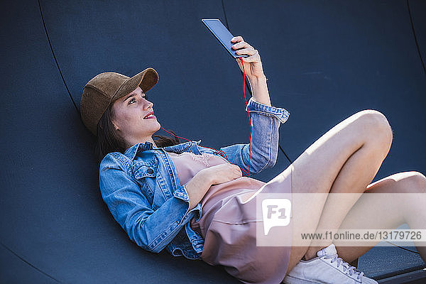 Junge Frau liegt im Freien mit Handy in der Hand