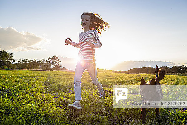 Mädchen mit einem Hund  das bei Sonnenuntergang über ein Feld läuft