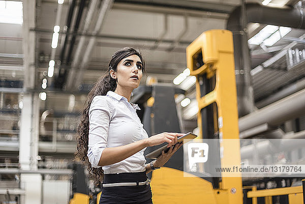 Woman with tablet in factory shop floor looking around