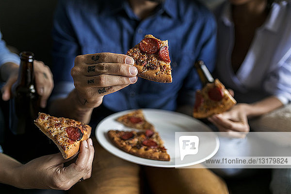 Nahaufnahme eines tätowierten Mannes mit Freunden  die ein Pizzastück in der Hand halten