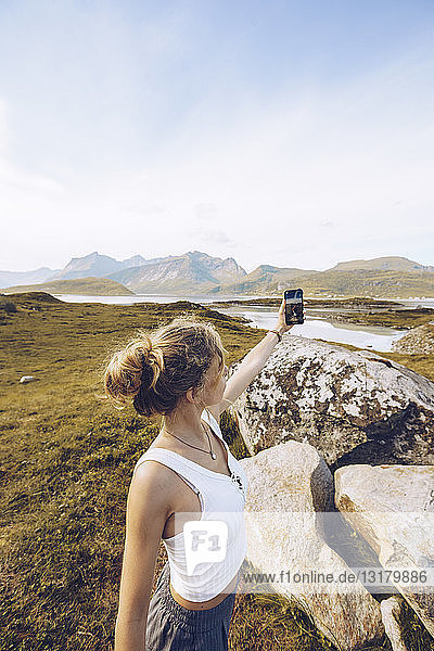 Norwegen  Lofoten  junge Frau  die in der Natur mit dem Smartphone Selfie betreibt