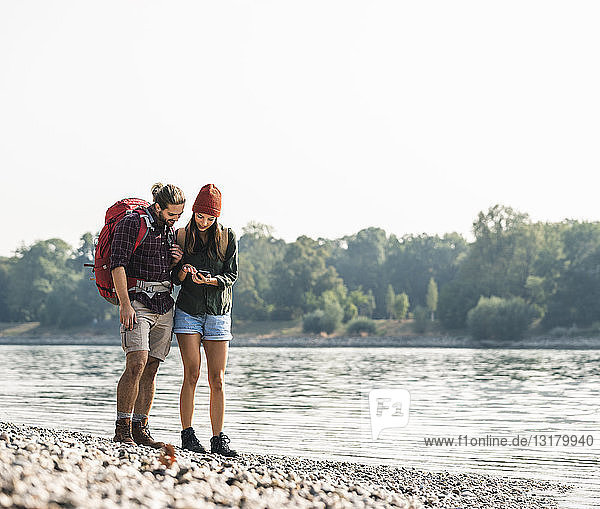 Young couple with backpacks at the riverside checking cell phone