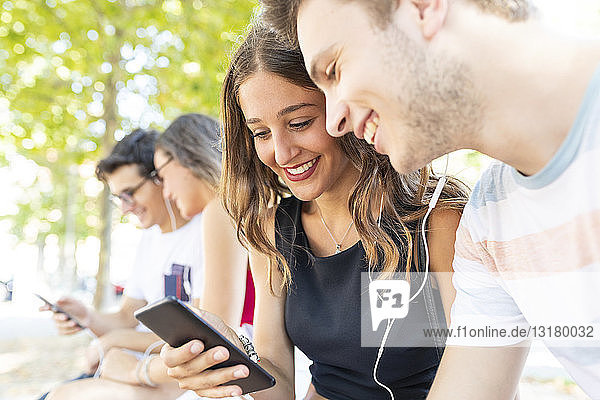 Eine Gruppe von Freunden in einem Park  die gemeinsam Spaß haben und Musik über Mobiltelefone hören