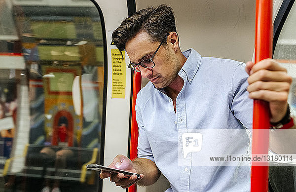 UK  London  businessman in underground train looking at cell phone