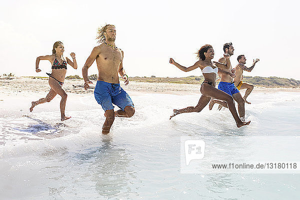 Group of friends having fun on the beach  running into the water