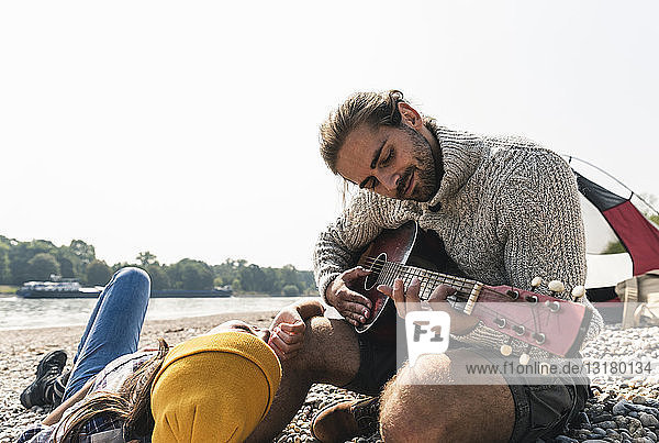 Glückliches junges Paar spielt Gitarre in einem Zelt am Flussufer