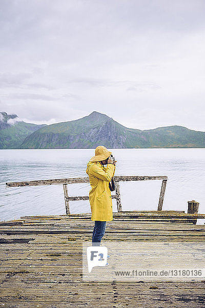 Norwegen  Senja  Mann steht auf einem baufälligen Steg an der Küste und macht ein Foto