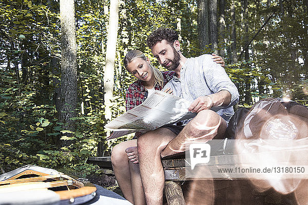 Junges Paar mit Karte und Kanu auf einem Steg an einem Waldbach sitzend