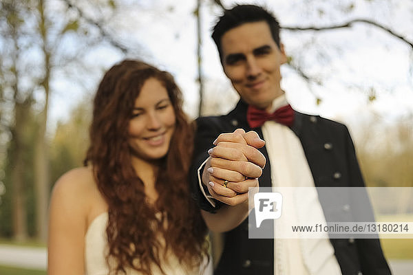 Glückliches Brautpaar steht im Park  hält Hände  zeigt Ehering