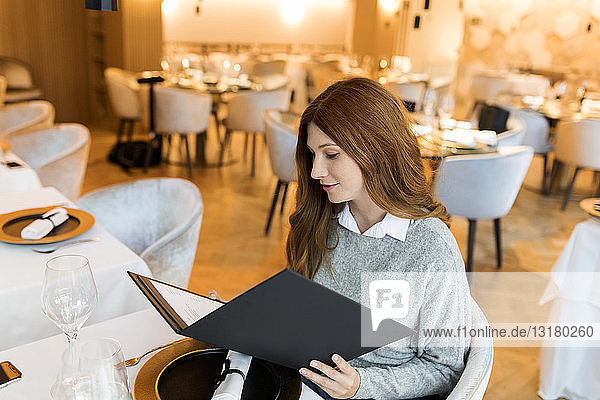 Frau  die in einem Restaurant am Tisch sitzt und die Speisekarte liest
