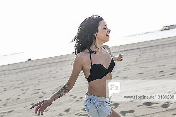 Happy young woman with tattoo and nose piercing running on the beach