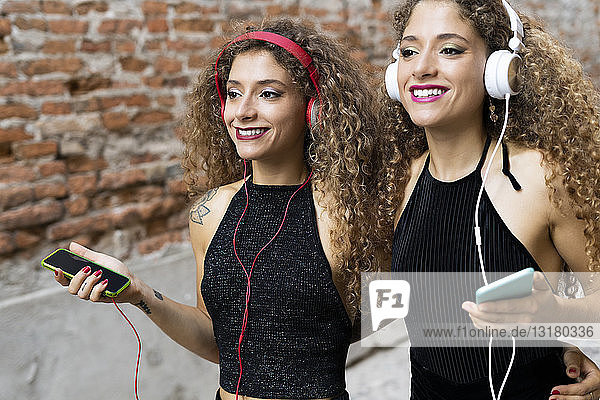 Porträt von glücklichen Zwillingsschwestern  die mit Kopfhörern und Mobiltelefonen Musik hören