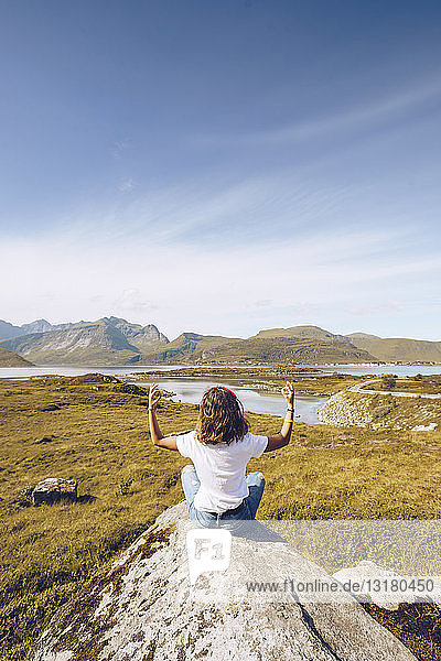 Norwegen  Lofoten  Rückenansicht einer jungen Frau  die auf einem Felsen sitzt und Yoga macht