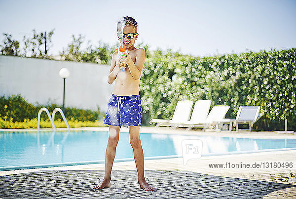 Junge am Poolrand mit Wasserpistole und Sonnenbrille