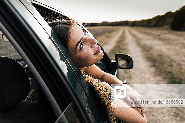 Lächelnde junge Frau lehnt sich aus dem Autofenster