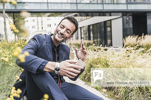 Businessman sitting outside  taking a break  listening music from his smartphone