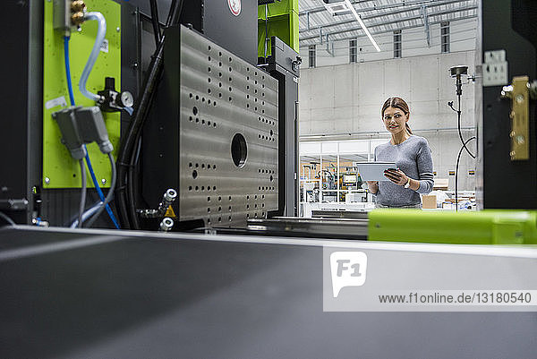 Geschäftsfrau in einem High-Tech-Unternehmen  die mit Hilfe eines digitalen Tabletts Produktionsmaschinen steuert