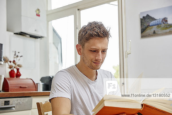 Smiling young man at home reading a book