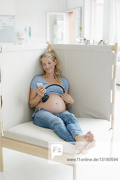 Lächelnde schwangere Frau hält Kopfhörer an ihren Bauch