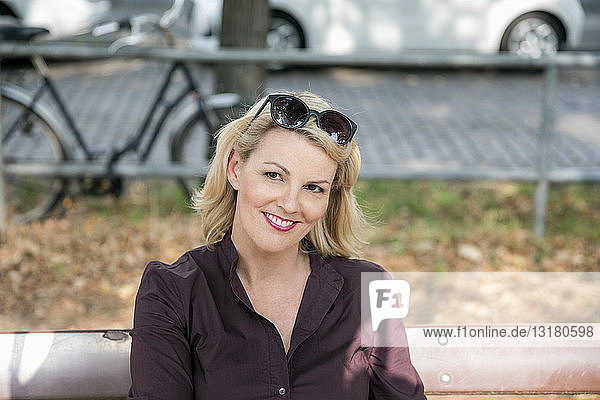 Porträt einer lächelnden  blonden  reifen Frau  die im Freien auf einer Bank sitzt