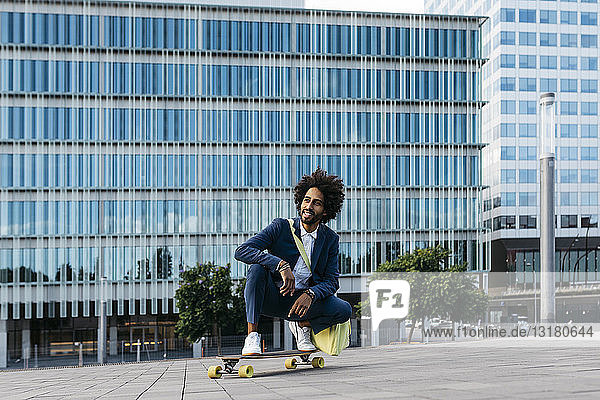 Spanien  Barcelona  junger Geschäftsmann kauert auf dem Skateboard in der Stadt