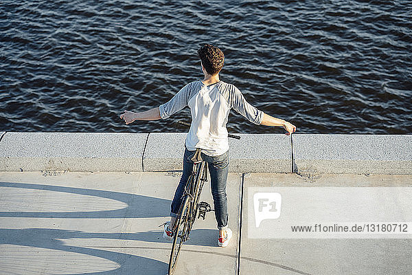 Junger Mann mit Pendler-Fixie-Fahrrad bei einer Pause am Flussufer