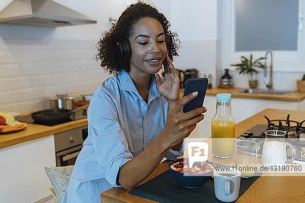 Frau mit Kopfhörern  die ein Smartphone in ihrer Küche benutzt