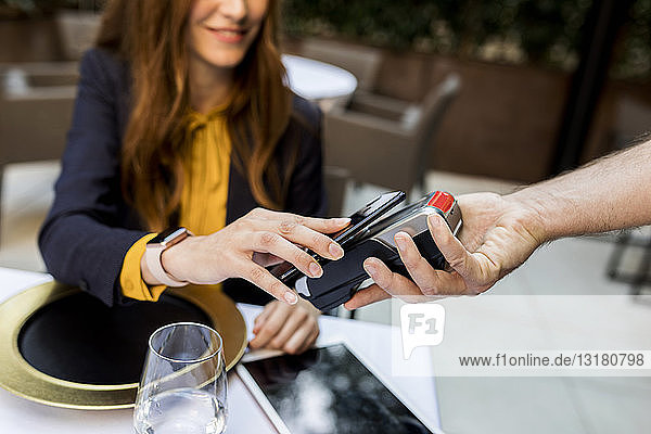 Frau  die in einem Restaurant mit einem Smartphone bezahlt