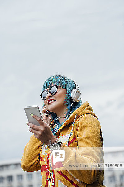 Portrait of young woman with dyed blue hair listening music with smartphone and headphones
