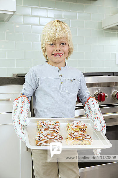 Porträt eines lächelnden Jungen  der ein Backblech mit Zimtbrötchen hält