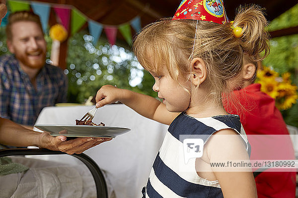 Kleines Mädchen isst Kuchen auf einer Geburtstagsgartenparty