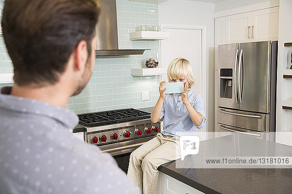 Son taking cell phone picture of father in kitchen