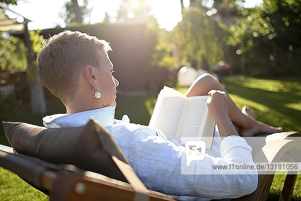 Frau auf Liegestuhl liest Buch im Garten