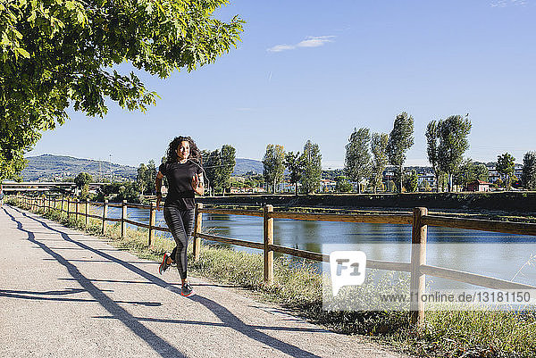 Sportliche junge Frau beim Laufen am Flussufer