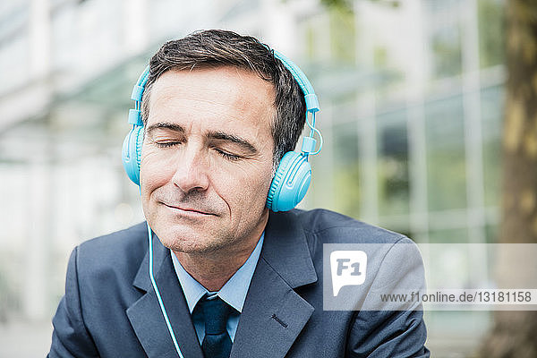 Geschäftsmann mit geschlossenen Augen  der in der Stadt mit Kopfhörern Musik hört