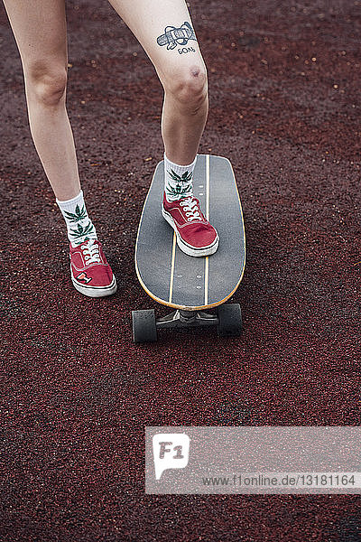 Frauenbeine in Socken und Turnschuhen auf Carver-Skateboard stehend