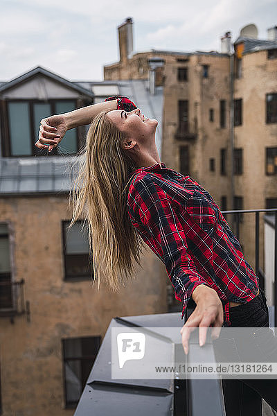 Lächelnde junge Frau steht auf dem Balkon und schaut nach oben