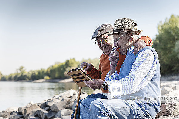Two old friends sitting by the riverside  using digital tablet