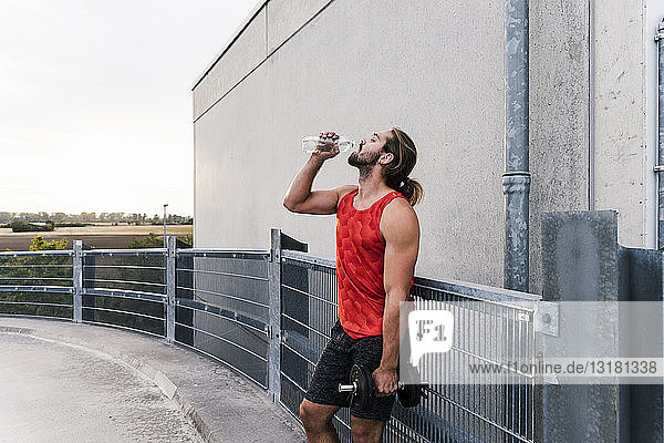 Young man drinking water after training with dumbells