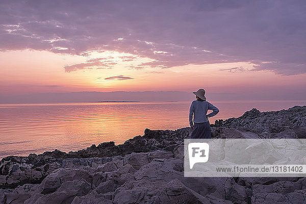 Kroatien  Istrien  Losinj  Frau steht bei Sonnenuntergang an Felsküste
